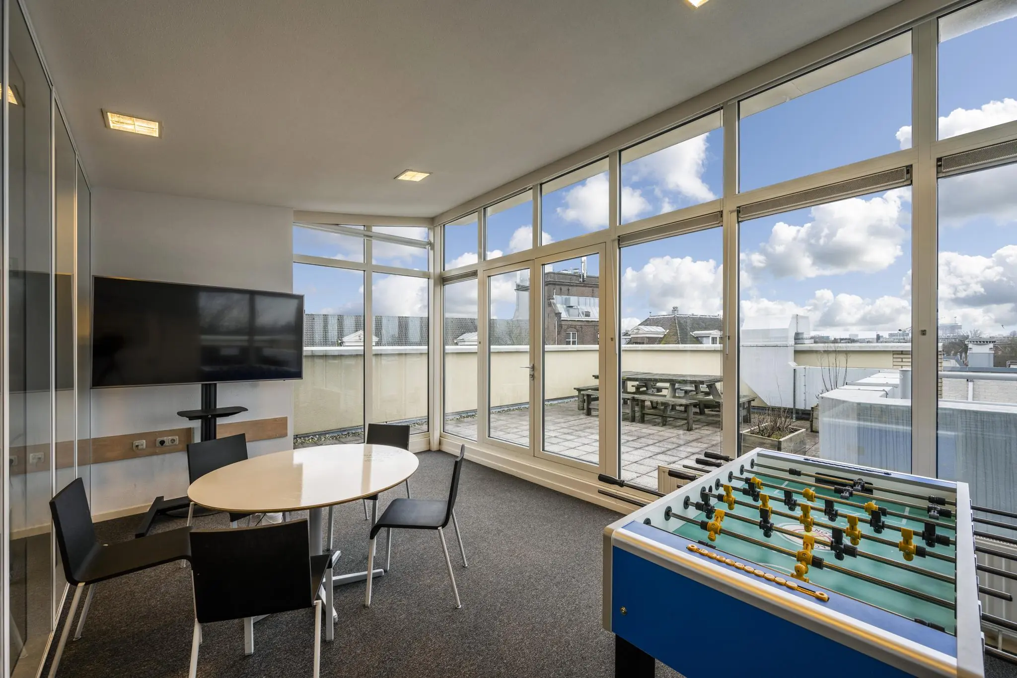 Moderne recreatieruimte met tafelvoetbal, vergadertafel, flatscreen-tv en uitzicht op een dakterras aan de Prins Hendrikkade.